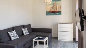 A modern living room with a grey sofa, a white side table, a painting of a sailboat, a white cabinet, and a mounted television. - Begovic Guest House - One-bedroom Apartment (Dubrovnik)