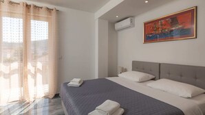 A hotel room with a large bed, a window with curtains, an air conditioning unit, and a painting on the wall. - Begovic Guest House - One-bedroom Apartment (Dubrovnik)