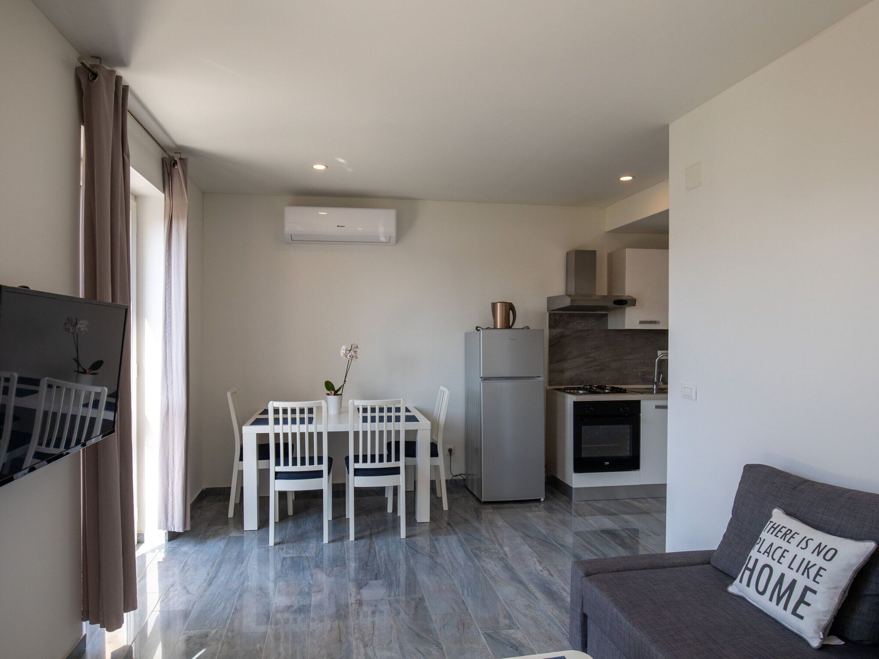 A modern apartment with a dining area, kitchenette, and a living room with a sofa and a decorative pillow.