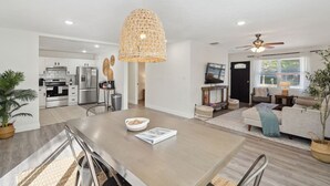 A modern kitchen with white cabinets, a dining area with a wooden table, and a living room with a sofa and a ceiling fan. - Coastal Getaway With Bikes & NEW Saltwater Pool (Sarasota)