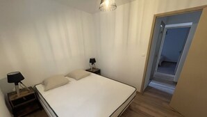 A bedroom with a single bed, a nightstand with a lamp, wooden flooring, and a door leading to another room. - Belle Maison Rénovée Avec Jardin, à 500m du Centre Village (Goudargues)