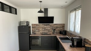 A modern kitchen with black cabinetry, a brick backsplash, a microwave, a toaster, and a coffee maker. - Belle Maison Rénovée Avec Jardin, à 500m du Centre Village (Goudargues)
