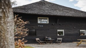 A rustic wooden cabin with a thatched roof, a small table, two chairs, and a bench. - Holiday Home in Former Barn in Ruinerwold (Ruinerwold)