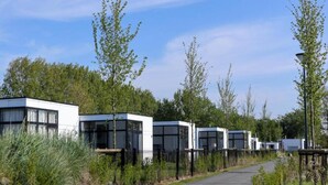 A row of modern, white, boxy buildings with large windows, surrounded by greenery and a clear sky. - Holiday Home in Former Barn in Ruinerwold (Ruinerwold)