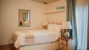 A neatly made bed with a bedside table, a mirror, and a shelf with a 'BE HAPPY' sign.