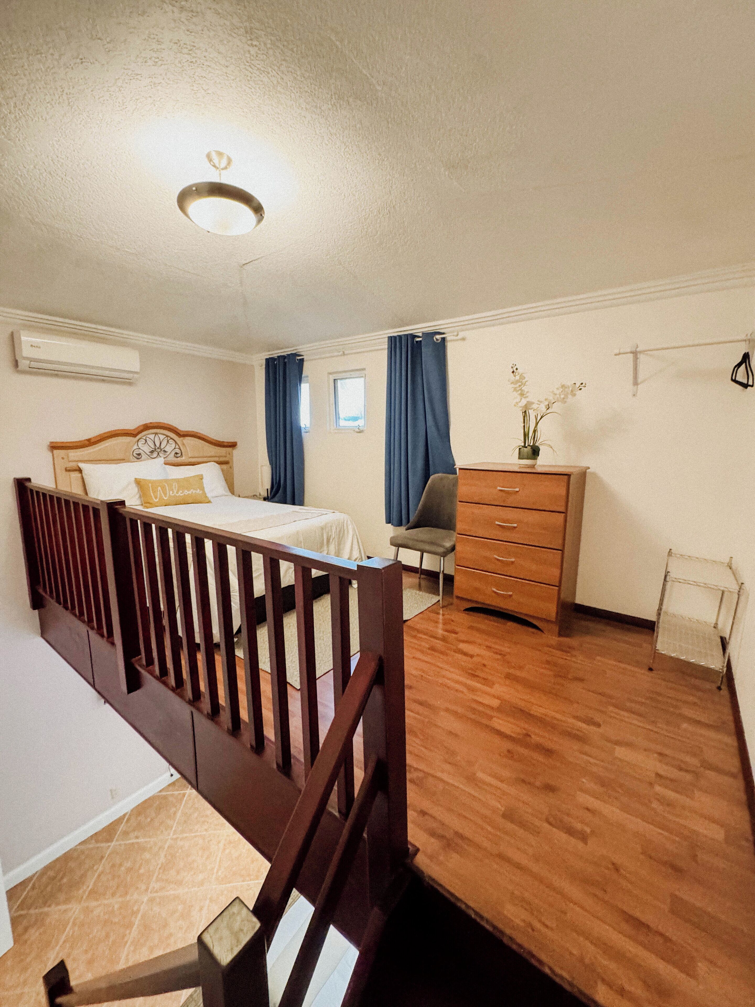 Quarto com cama de madeira, cômoda, cadeira e mesa pequena.