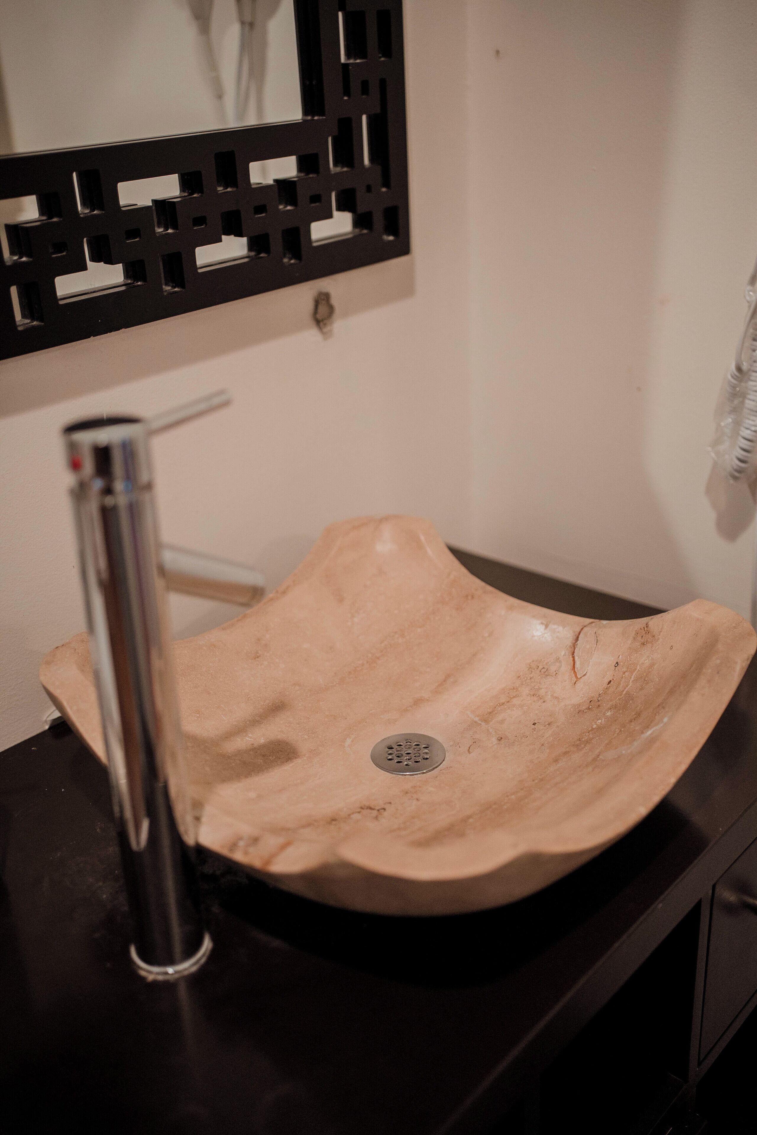 Un bagno con un lavandino in ceramica beige, un rubinetto cromato e un pannello decorativo nero sopra il lavandino.
