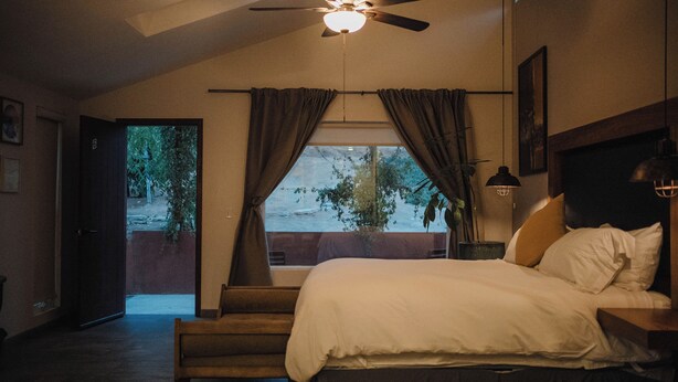 A bedroom with a bed, a ceiling fan, a window with curtains, and a view of the outdoors. - Tierra Mia Hacienda Ruta del Vino (Valle de Guadalupe)