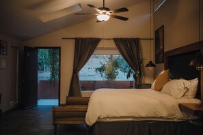 Un dormitorio con cama, ventilador de techo, ventana con cortinas y vistas al exterior.