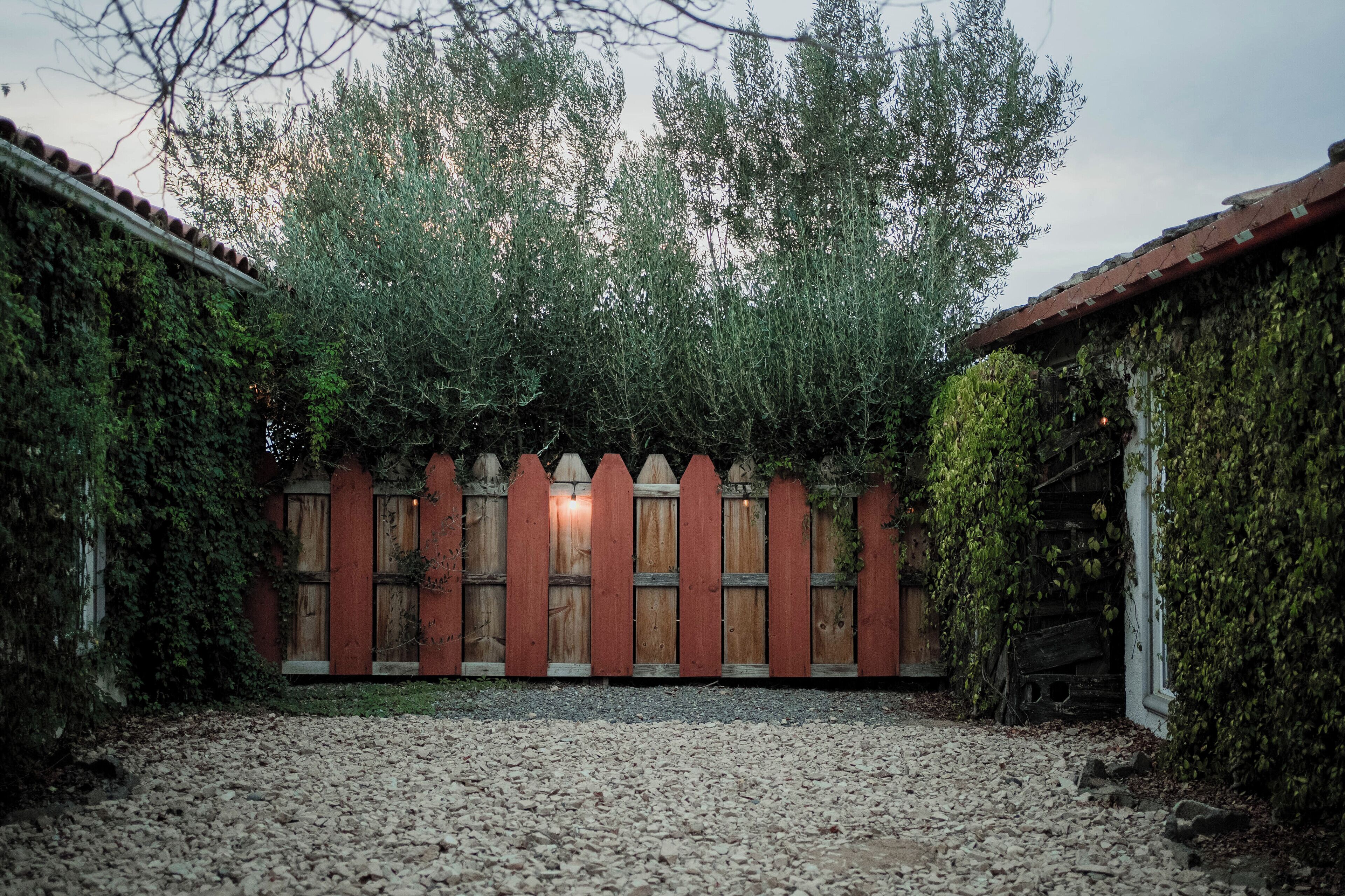 A courtyard with a gravel path, wooden fence, and a wooden building with a tiled roof.