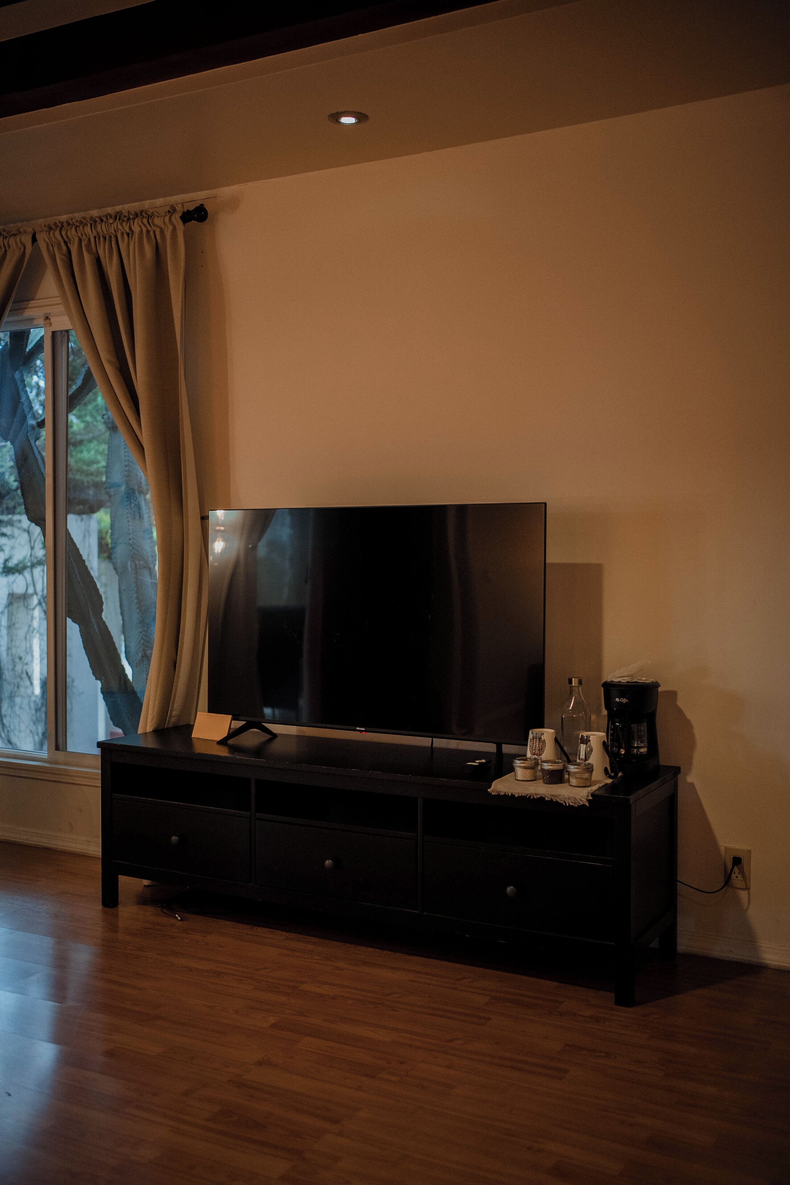 Un salon moderne avec un grand téléviseur à écran plat posé sur un meuble TV en bois foncé, une machine à café et une petite table agrémentée d’objets décoratifs.
