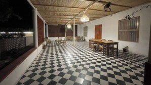 Un espace extérieur abrité, doté d’un sol à carreaux, d’un plafond en bois et d’une table à manger avec des chaises.