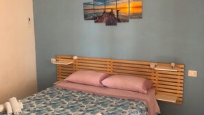 Une chambre avec un lit en bois, un mur bleu et un tableau représentant un coucher de soleil.
