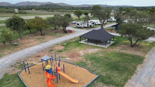 A playground with a slide and climbing structures, surrounded by a grassy area and trees.