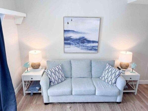 A modern living room with a light grey sofa, two matching nightstands, and a framed abstract painting on the wall.