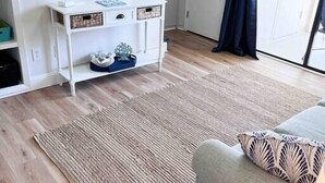 A modern living room with a wooden floor, a grey sofa, a round mirror, and a white console table with decorative items. - Beautifully Decorated Beachfront Condo! (Orange Beach)