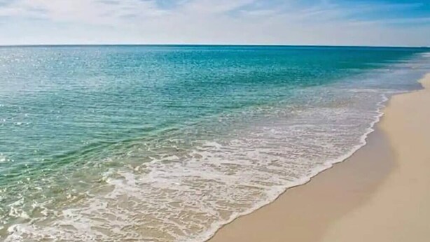 A beach with clear turquoise water and a sandy shore. - Beautifully Decorated Beachfront Condo! (Orange Beach)