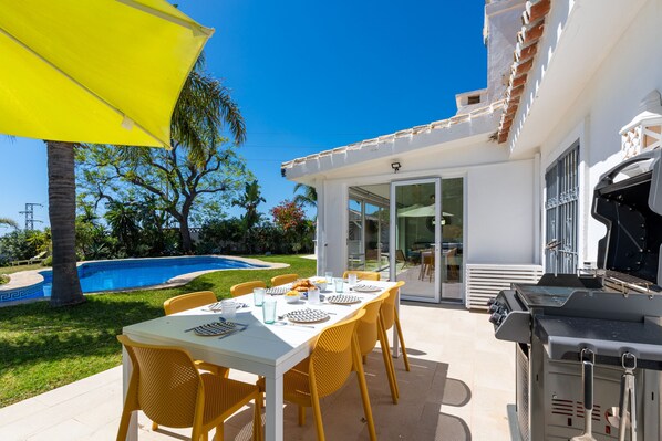 An outdoor patio with a dining table, yellow chairs, and a grill.