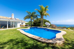 A swimming pool with a clear blue water feature, surrounded by a well-maintained lawn and palm trees.