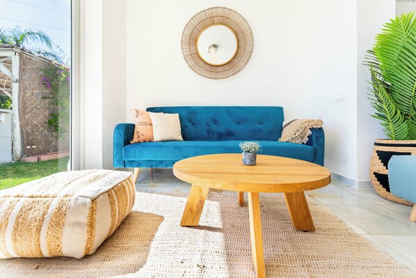 A modern living room with a blue sofa, a round wooden coffee table, and a large mirror on the wall.