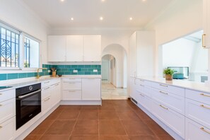 A modern kitchen with white cabinetry, a Bosch oven, teal backsplash, and a view to the living area.
