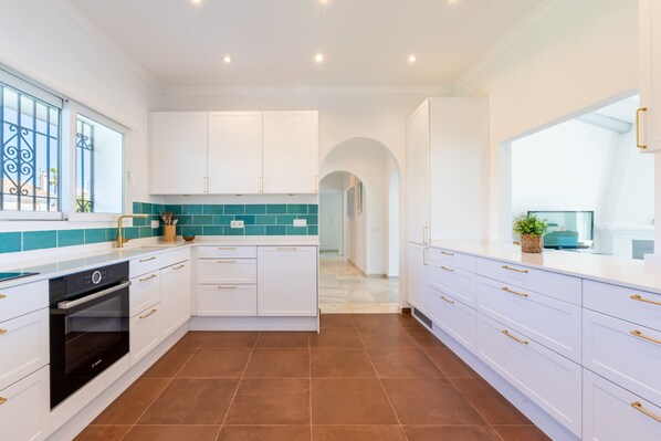 A modern kitchen with white cabinetry, a Bosch oven, teal backsplash, and a view to the living area.