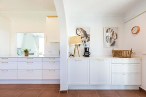 A modern kitchen with white cabinetry, a coffee maker, and decorative wall art.