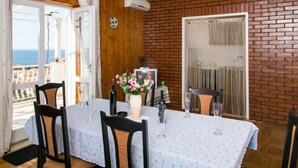 A dining area with a table set for four, a vase of flowers, and a view of the sea through a glass door. - Apartment Angelina - Three Bedroom Apartment With Balcony and Sea View (Dubrovnik)
