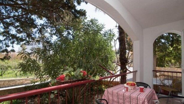 A balcony with a table set for two, surrounded by greenery and a red railing. - Apartments Boguvila - Two-bedroom Standard Apartment With Terrace - (Supetar)