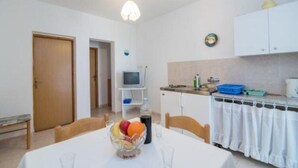 A compact kitchen with white cabinets, a small TV, and a dining area with a table set for two. - Apartments Boguvila - Two-bedroom Standard Apartment With Terrace - (Supetar)
