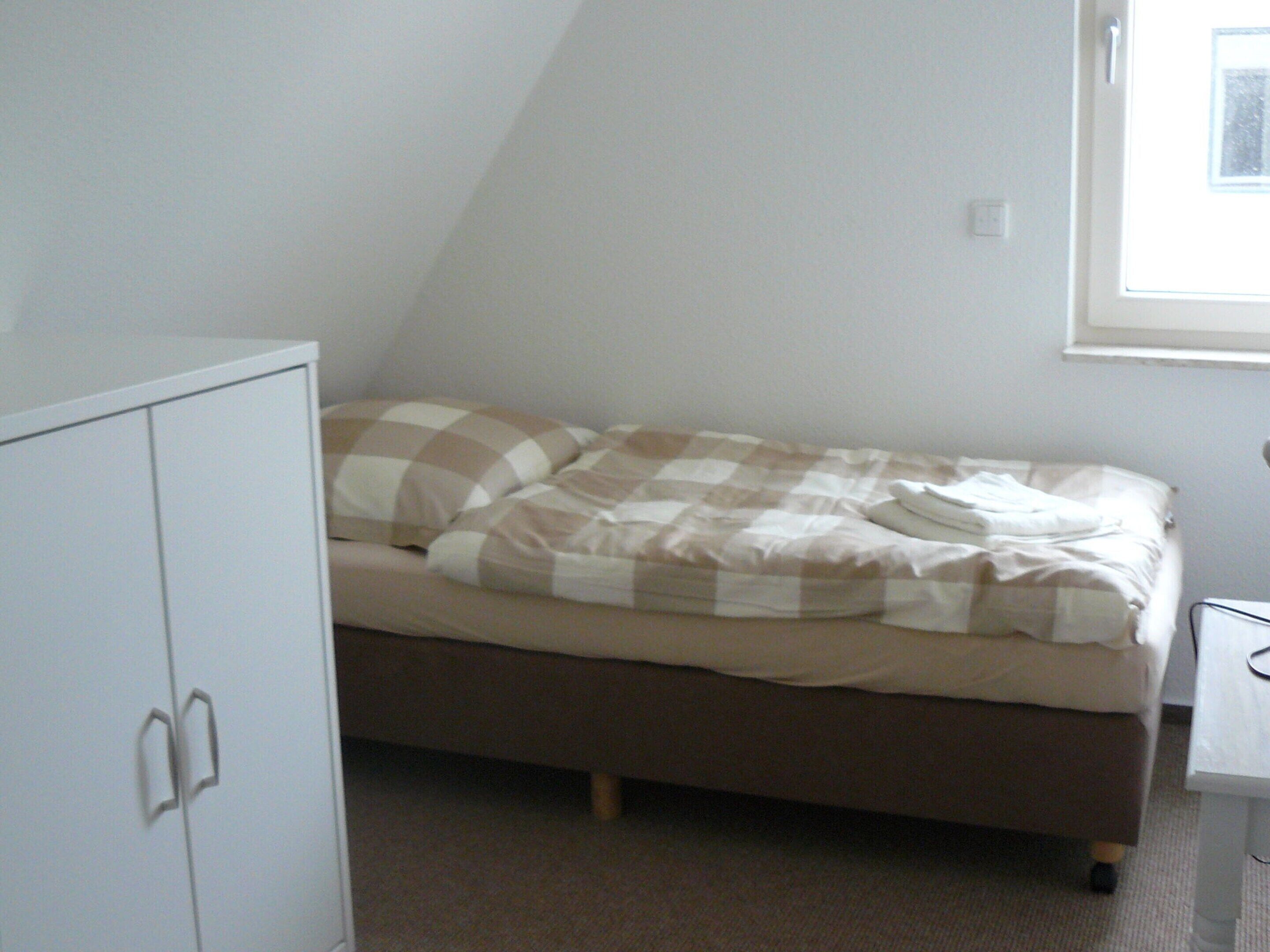 A small, single-bed room with a plain white wardrobe and a window providing natural light.