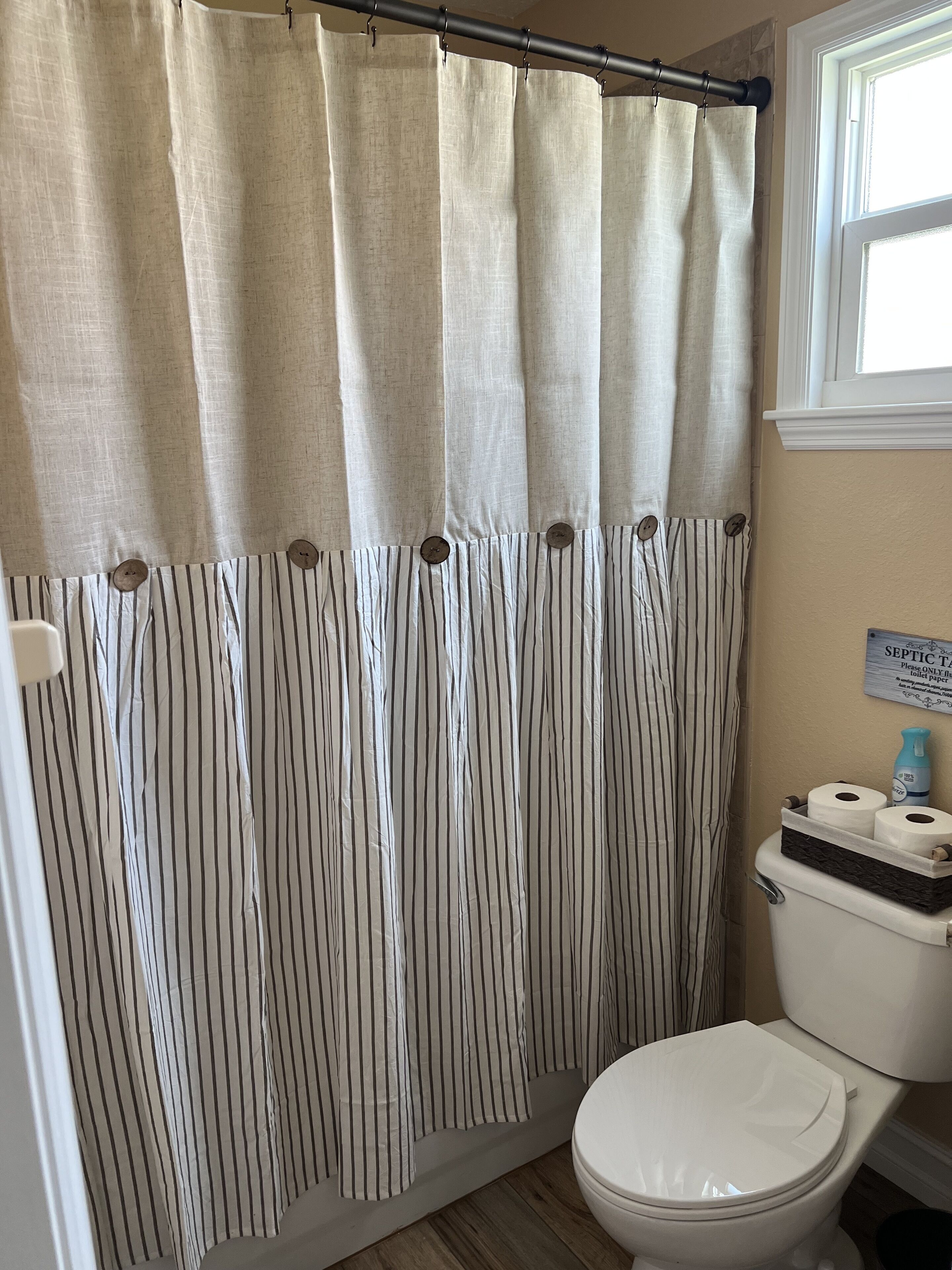 Et badeværelse med en stribet bruseforhæng, toilet og et skilt, der angiver, at toiletpapir skal bruges.
