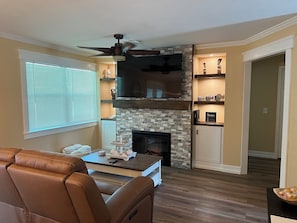 Cozy up by the fireplace in this inviting living room, featuring a mounted TV and comfortable leather sofa.