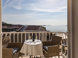 A balcony with a table and two wicker chairs, overlooking a body of water and distant hills. - Rooms Tupina by Paulina - Superior Double Room With Balcony and Sea View (Zupa dubrovacka)