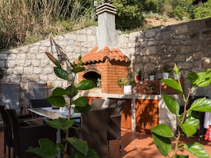 An outdoor patio with a brick oven, wicker furniture, and potted plants. - Rooms Tupina by Paulina - Superior Double Room With Balcony and Sea View (Zupa dubrovacka)