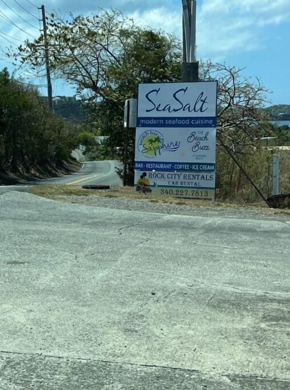 A roadside sign for 'SeaSalt' with a modern seafood cuisine logo, 'Beach Buzz' logo, and mentions a bar, restaurant, coffee, and ice cream. It also advertises 'Rock City Rentals' with a contact number.