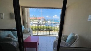 Un balcón con vista a un puerto deportivo y edificios. Hay una mesa roja y dos sofás.