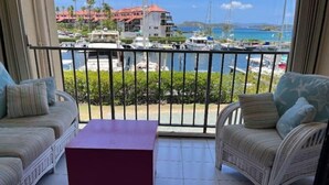 Un balcón con muebles de mimbre y una pequeña mesa, con vistas a un puerto deportivo con barcos y edificios.