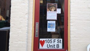 Une porte rouge avec une pancarte indiquant « 105, rue F, unité B » et un symbole en forme de cœur.