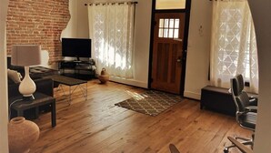 Una sala de estar con pared de ladrillo, televisor, sofá, mesa de centro y puerta.