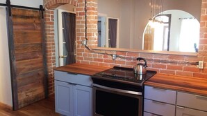 Una cocina con pared de ladrillo, encimera de madera y electrodomésticos de acero inoxidable, además de un espejo grande.