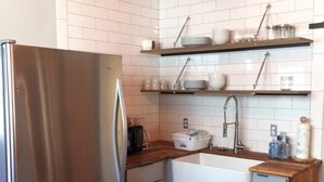 Una cocina moderna con refrigerador de acero inoxidable, gabinetes de madera, encimera de madera y salpicadero de azulejos blancos.