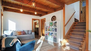 A living room with a sofa, a bookshelf, and a staircase. - Our sunny, solar-powered home is located on the biking path that leads to Salida’s quaint downtown. The house has a rural feel and fantastic panoramic views, but is just 3 miles from all the restaurants, galleries, shops, and parks of Salida. (Salida)