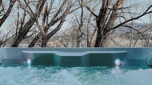 A hot tub with a view of leafless trees and a distant landscape. - Our sunny, solar-powered home is located on the biking path that leads to Salida’s quaint downtown. The house has a rural feel and fantastic panoramic views, but is just 3 miles from all the restaurants, galleries, shops, and parks of Salida. (Salida)