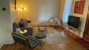 Una sala de estar con un sofá, una silla, una mesita de centro, un televisor y una lámpara de pie.