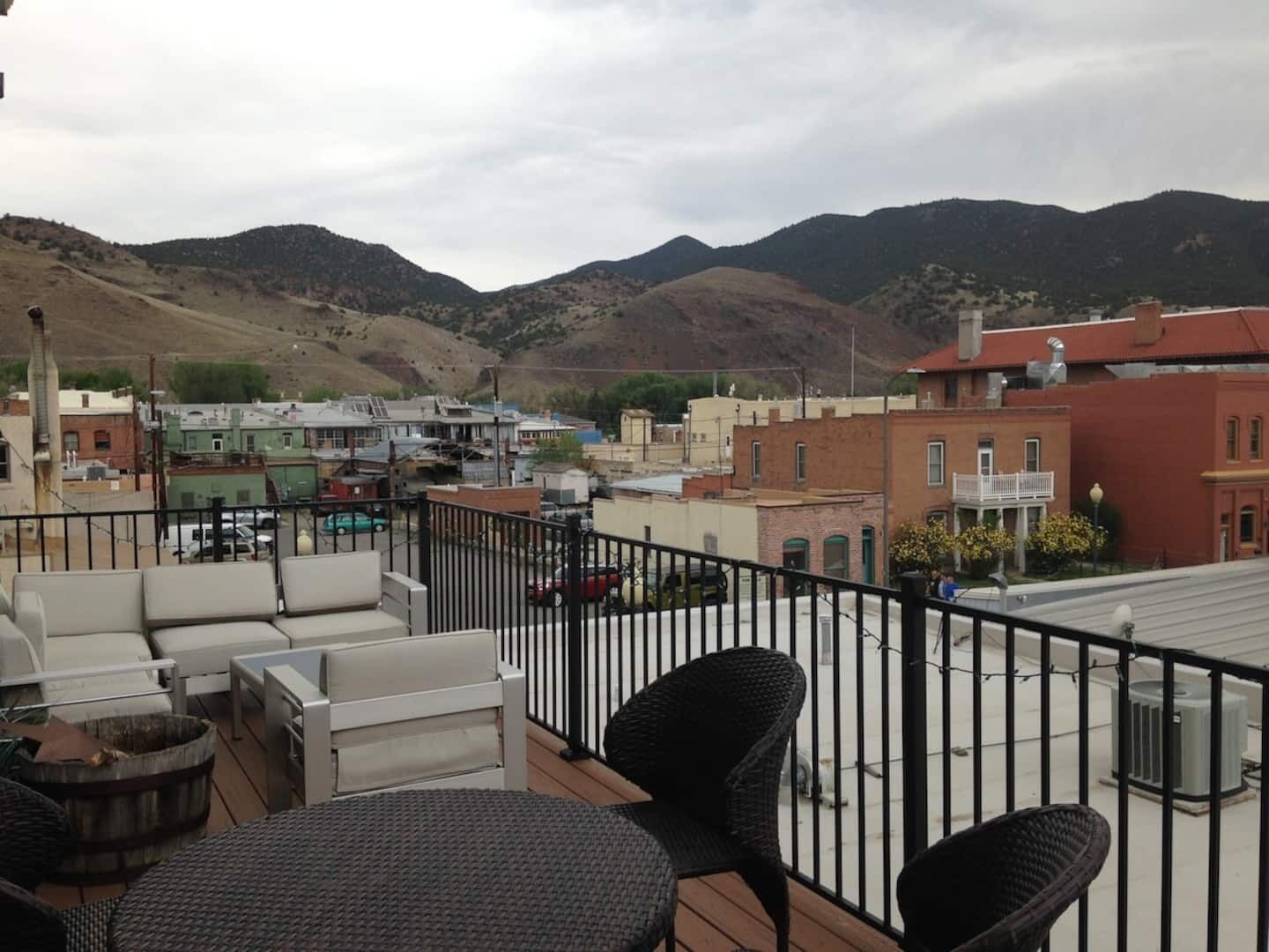 Una terraza en la azotea con mobiliario exterior, vistas a un pueblo y montañas al fondo.