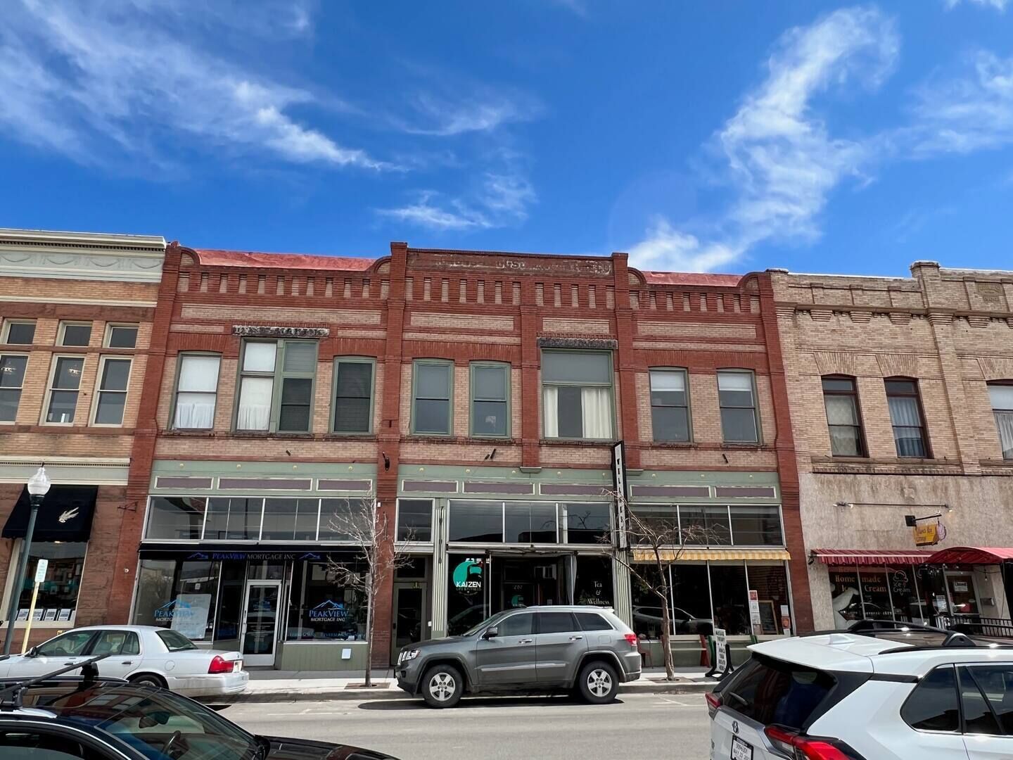 A street view with a row of brick buildings, including a visible storefront with a sign that reads "PeakView Mortgage Inc."