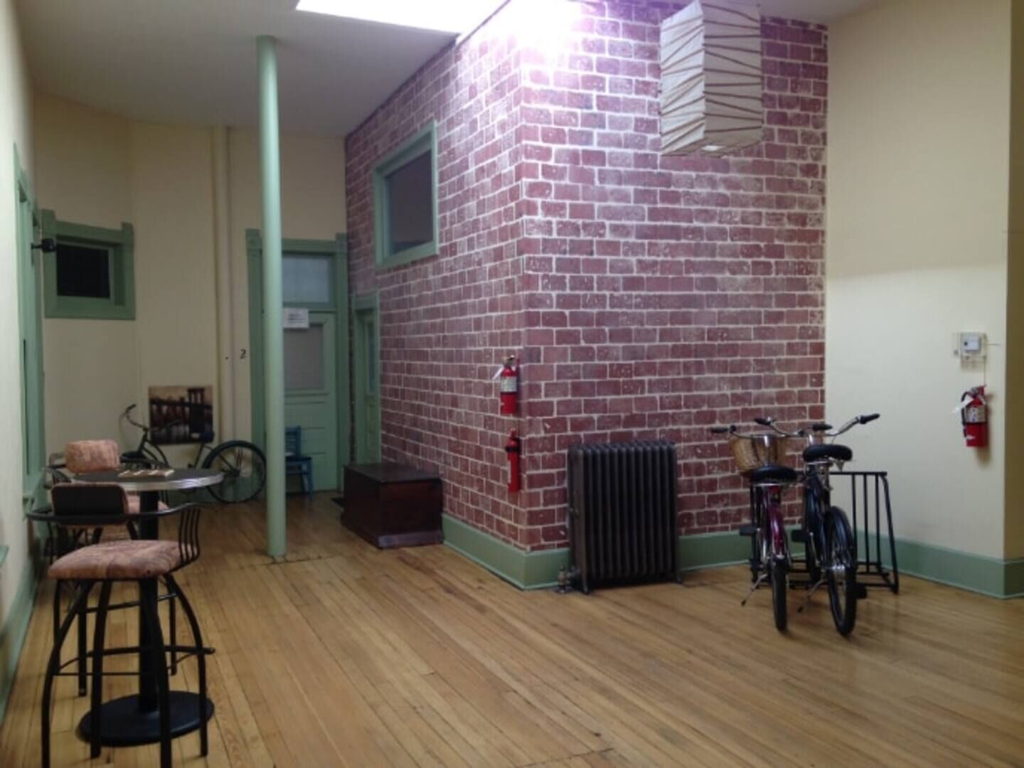 Una habitación con pared de ladrillo, suelo de madera, un radiador, una bicicleta y un taburete.