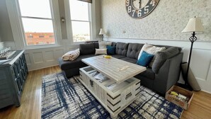 A living room with a grey sofa, a coffee table, a patterned rug, and a large wall clock. - 2nd story condo overlooking the F Street Pedestrian mall, downtown Salida! (Salida)