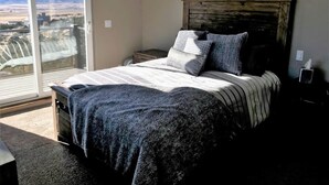 Une chambre à coucher avec un grand lit, une tête de lit en bois, des lampes de chevet et une vue sur l’extérieur, accessible par une porte-fenêtre coulissante.